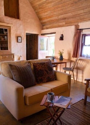 A cozy living room with a sofa, a small table, and a window. - Historical Thatched Cottage @ Multi-Award-Winning Cnoc Suain (Galway)