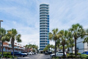 Un grand hôtel à plusieurs étages, doté de balcons, entouré de palmiers et bordé de voitures garées.