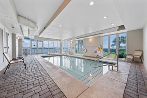 Une piscine avec un sol en briques, un poste de surveillance pour le sauveteur et un banc.