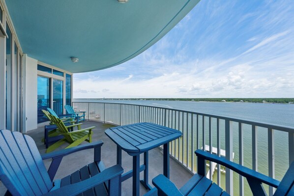 Un balcon avec des fauteuils Adirondack bleus, une petite table et une vue sur une étendue d’eau.
