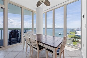 Un balcon avec une table et des chaises pour prendre les repas, de grandes fenêtres et une vue sur l’eau et le port de plaisance.