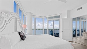 A large bed with white bedding, a view of the water, and a balcony with a chair. - Stunning Lagoon Front Views | Pool | Fishing Pier & Boat Slips (Gulf Shores)
