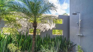 A modern outdoor shower area with a palm tree and various plants.