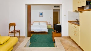 A compact hotel room with a bed, a TV, a small kitchenette, and a yellow sofa.
