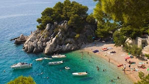 A coastal beach with boats, people, and a rocky outcrop with trees. - Studio apartment in Brela with Seaview, Terrace, Air condition, WIFI (201-8) (Brela)