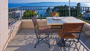 An outdoor patio with a table, chairs, and an umbrella. It overlooks a body of water and a distant coastline. - Studio apartment in Brela with Seaview, Terrace, Air condition, WIFI (201-8) (Brela)