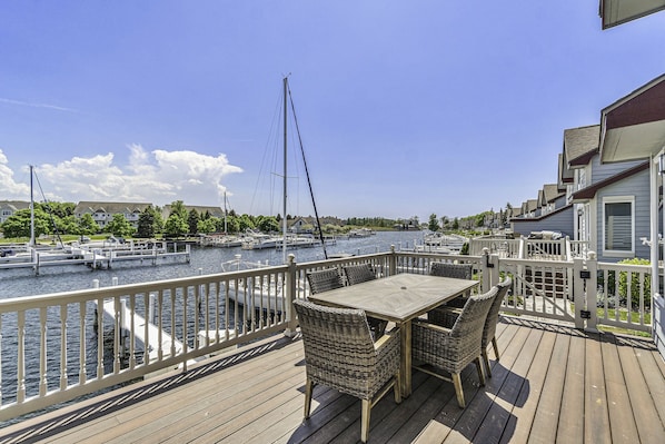 A wooden deck with a table and chairs overlooking a marina with boats.