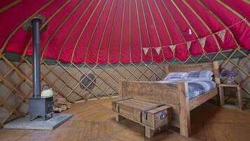 A cozy interior of a traditional yurt with a wooden bed, a small table, and a wood stove.