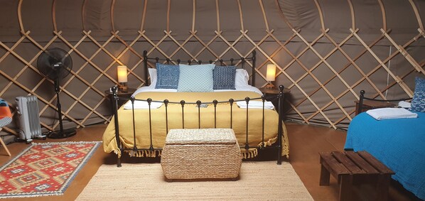 Ein gemütliches Zimmer mit einem Bett, einem kleinen Tisch, einer Bank, einem Ventilator und einer Heizung.