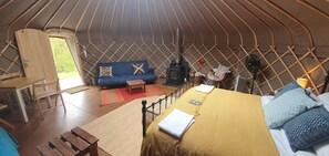 Ein gemütliches Innenleben eines Jurtenzeltes mit einer Couch, einem Bett, einem kleinen Tisch und einem Heizgerät.