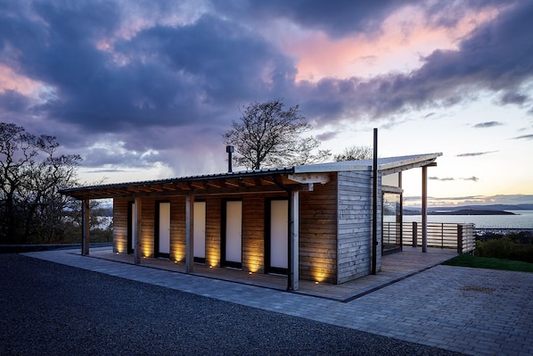 A modern outdoor structure with a wooden facade and a covered seating area, overlooking a body of water.