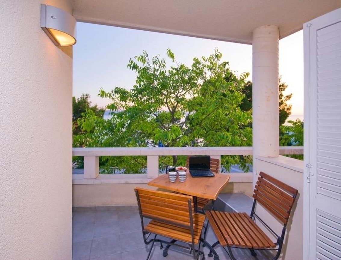 Ein Balkon mit Holztisch und Stühlen, einem Laptop und einem kleinen Bücherstapel.