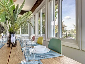 A dining area with a wooden table set for two, a vase with green foliage, and a view of the outdoors through large windows. - Dog friendly summer escape: Waterfront, Game Room, Hot Tub (Palm Coast)