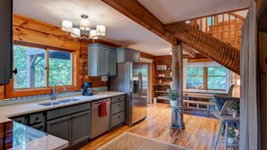 A modern kitchen with wooden beams, a large island, and a view to the outdoor deck. - Heritage Hill Cabins (Banner Elk)