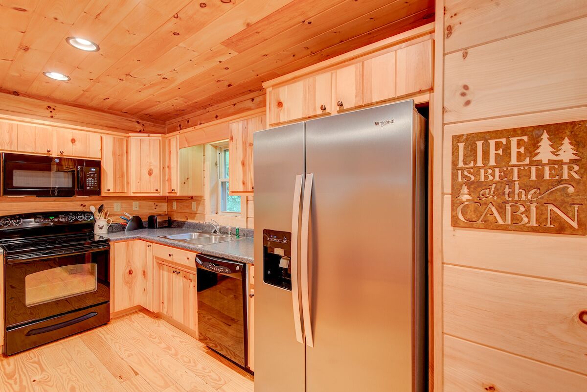 Una cucina in stile baita con mobili in legno, un frigorifero in acciaio inossidabile, un forno a microonde, un forno e una lavastoviglie.
