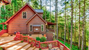 A log cabin with a deck, outdoor seating, and a view of the surrounding forest. - Heritage Hill Cabins (Banner Elk)