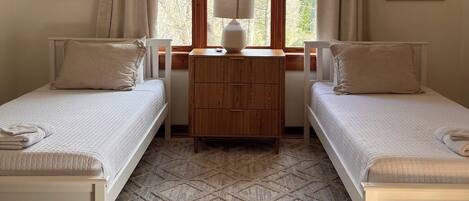 A room with two beds, a ceiling fan, a window with curtains, and artwork on the walls.