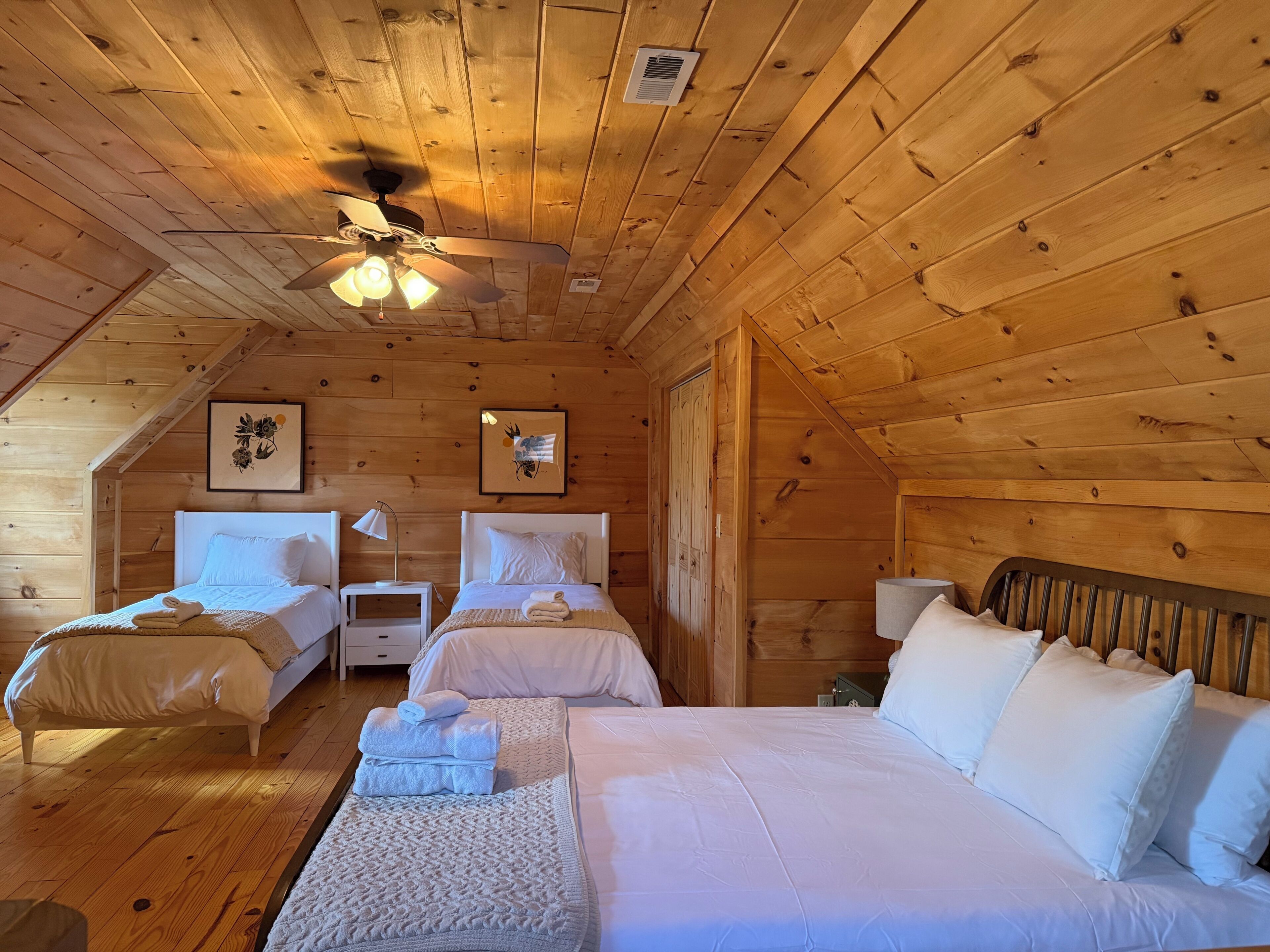 Een slaapkamer in een houten hut met twee bedden, een plafondventilator en een ingelijst foto aan de muur.