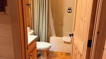 Baño de una cabaña de madera con inodoro, lavabo y ducha.