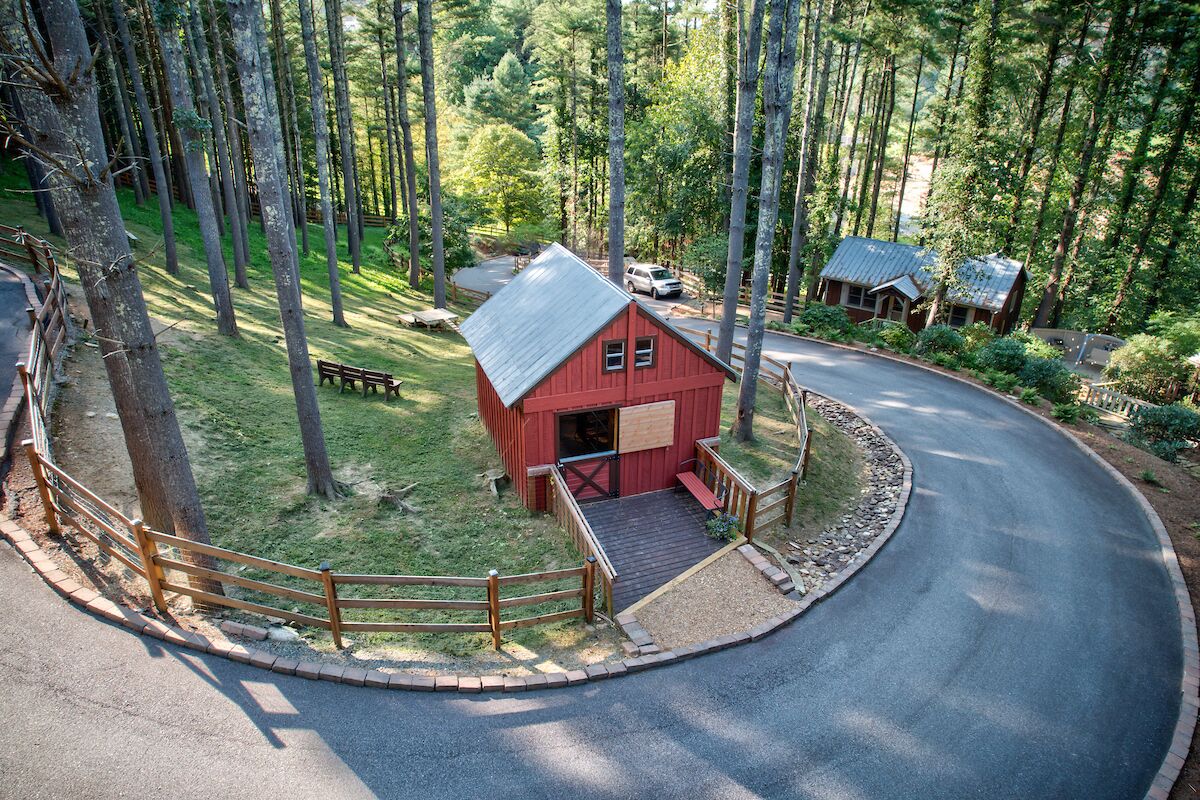 Une cabane rouge avec un porche, entourée d’une clôture en bois et de grands arbres.