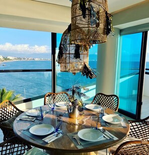 A dining table set for two with a view of the sea and a cityscape.