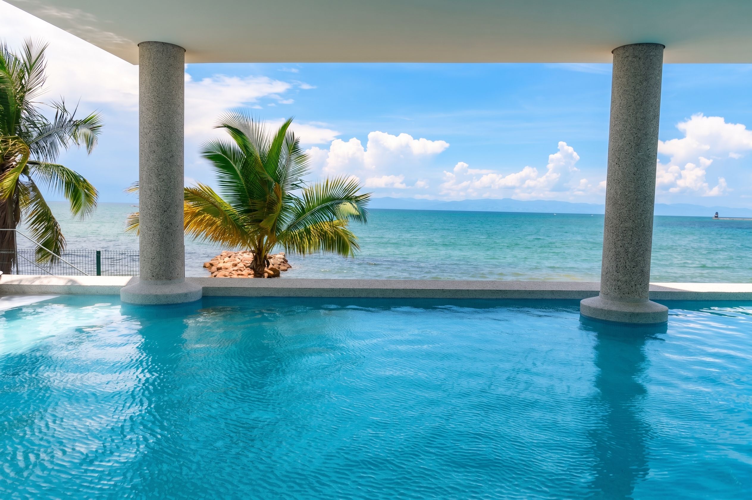 A pool with clear blue water, surrounded by palm trees and a view of the ocean.