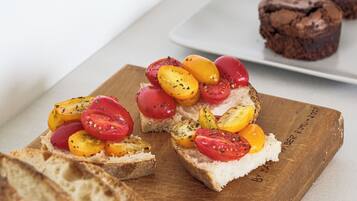Une planche en bois sur laquelle sont disposées des tranches de pain garnies de tomates et d’herbes, et une assiette de muffins au chocolat en arrière-plan.