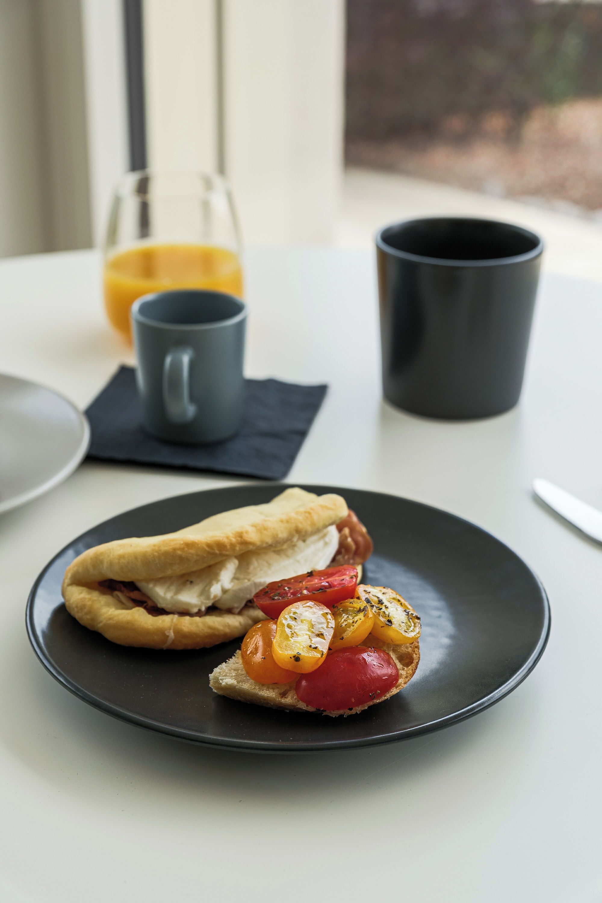 Un sandwich sur une assiette, accompagné d’un verre de jus d’orange et d’une tasse posée sur une table.