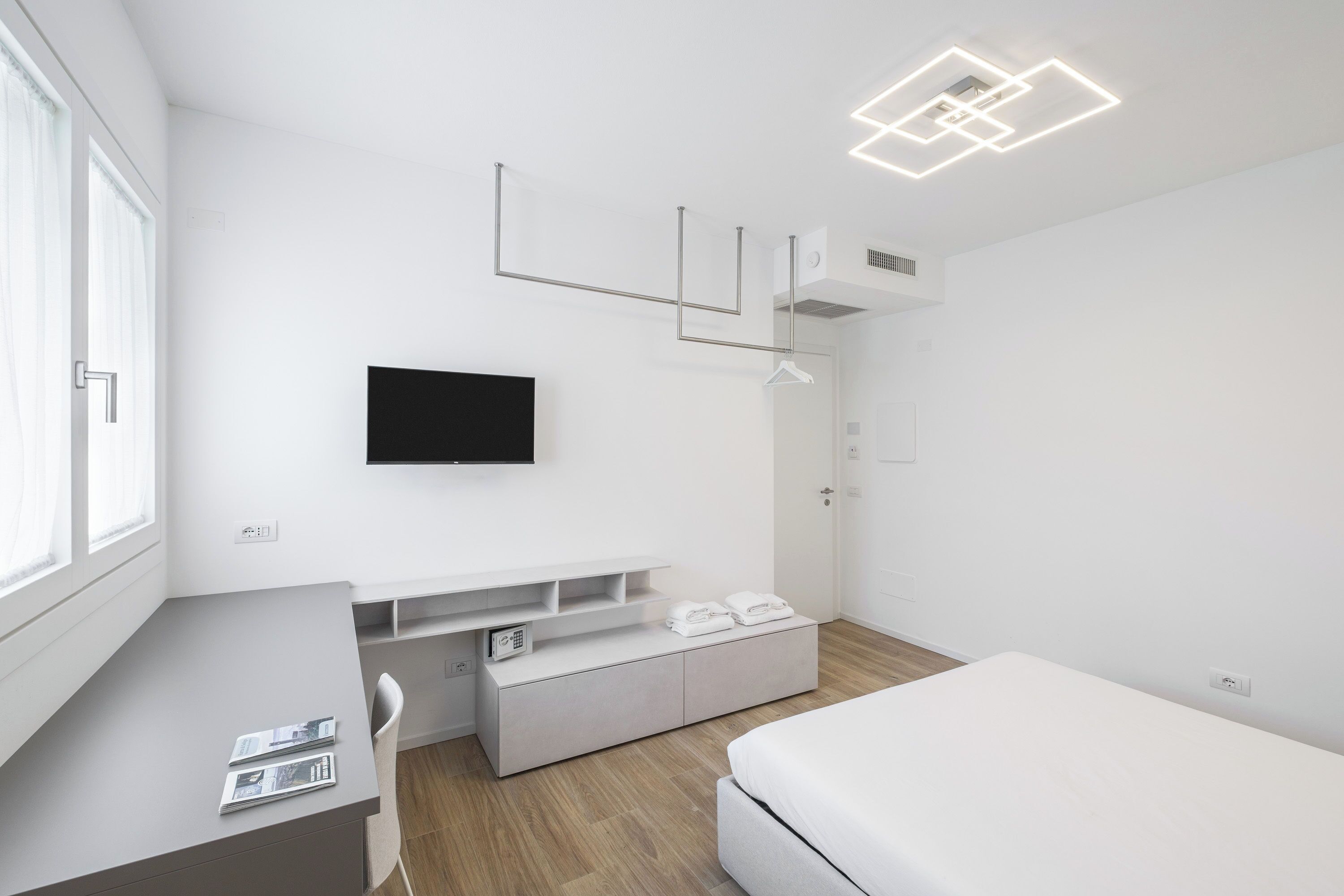 Una habitación de hotel moderna con televisión de pantalla plana, un escritorio con silla, una cama y un banco empotrado con toallas.