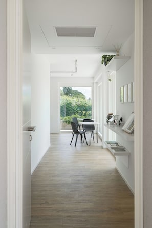 Un intérieur moderne avec un plancher en bois, des murs blancs, un coin repas avec des chaises et une vue à travers une porte vitrée.