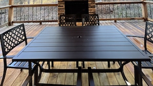Un área de estar al aire libre techada, con chimenea de piedra, terraza de madera y vista a árboles.