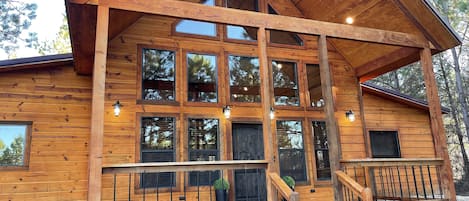 Situated in a wooded area, this cabin features a charming front porch with stairs and lantern-style lights.