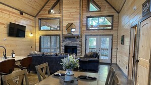 Un interior de cabaña acogedor, con comedor, chimenea y ventanas amplias.