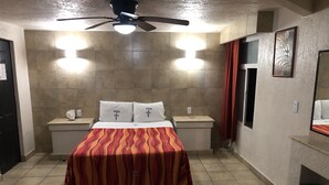 Habitación de hotel con cama, dos mesitas de noche, ventilador de techo y aplique de pared.