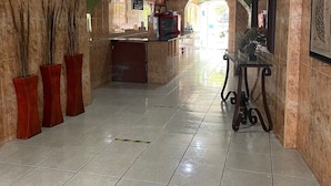 Un vestíbulo con una mesa de recepción, una zona de espera con un banco y un suelo de baldosas.