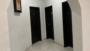Un pasillo con tres puertas negras, paredes blancas y suelo de baldosas.