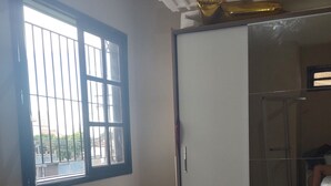 A room with a window, a pink stool, a tiled floor, and a bed with a floral bedspread. - Casa de Família Próx a Praia do Centro (Rio das Ostras)