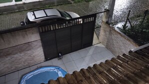 A residential area with a gated entrance, a swimming pool, and a parked car. - Casa de Família Próx a Praia do Centro (Rio das Ostras)
