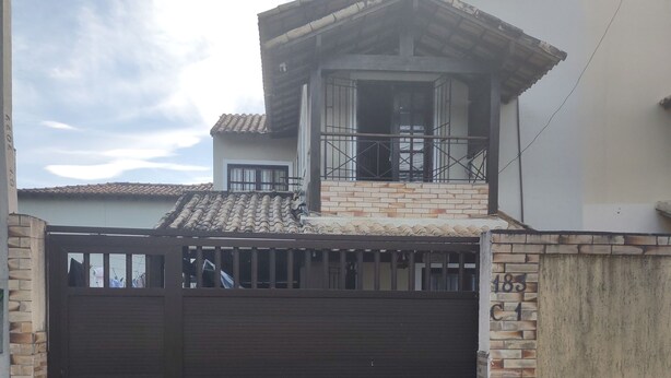 A residential building with a gated entrance, a small balcony, and a tiled driveway. - Casa de Família Próx a Praia do Centro (Rio das Ostras)