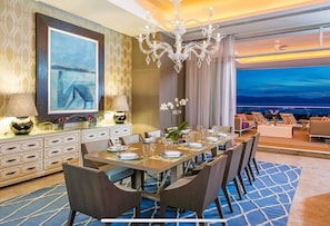 Enjoy meals in this stylish dining area with ocean views, a long table, modern chairs, and a sofa.
