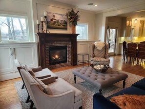 A living room with a fireplace, a sofa, a chair, and a dining area in the background. - 4624 Luxury family home (Urbandale)