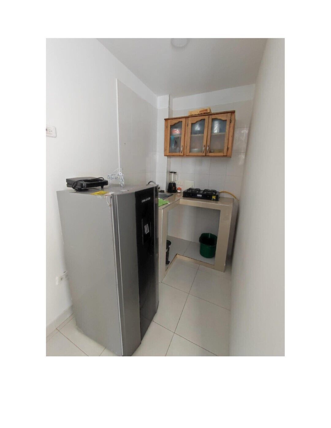 A compact kitchen with a refrigerator, a sink, and wooden cabinets.