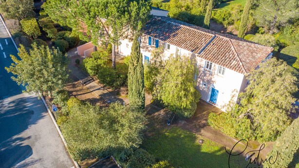 Une vue aérienne d’une maison entourée d’une végétation luxuriante, avec une allée pavée menant à l’entrée.