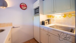 Une cuisine de taille réduite avec des meubles blancs, un four à micro-ondes, un grille-pain et une horloge murale.