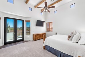 Een slaapkamer met een groot bed, een plafondventilator, een televisie aan de muur en uitzicht op de woestijn door de schuifdeuren.