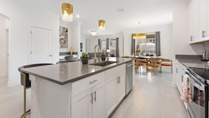 Una cocina moderna con una isla grande, armarios blancos e iluminación colgante dorada.