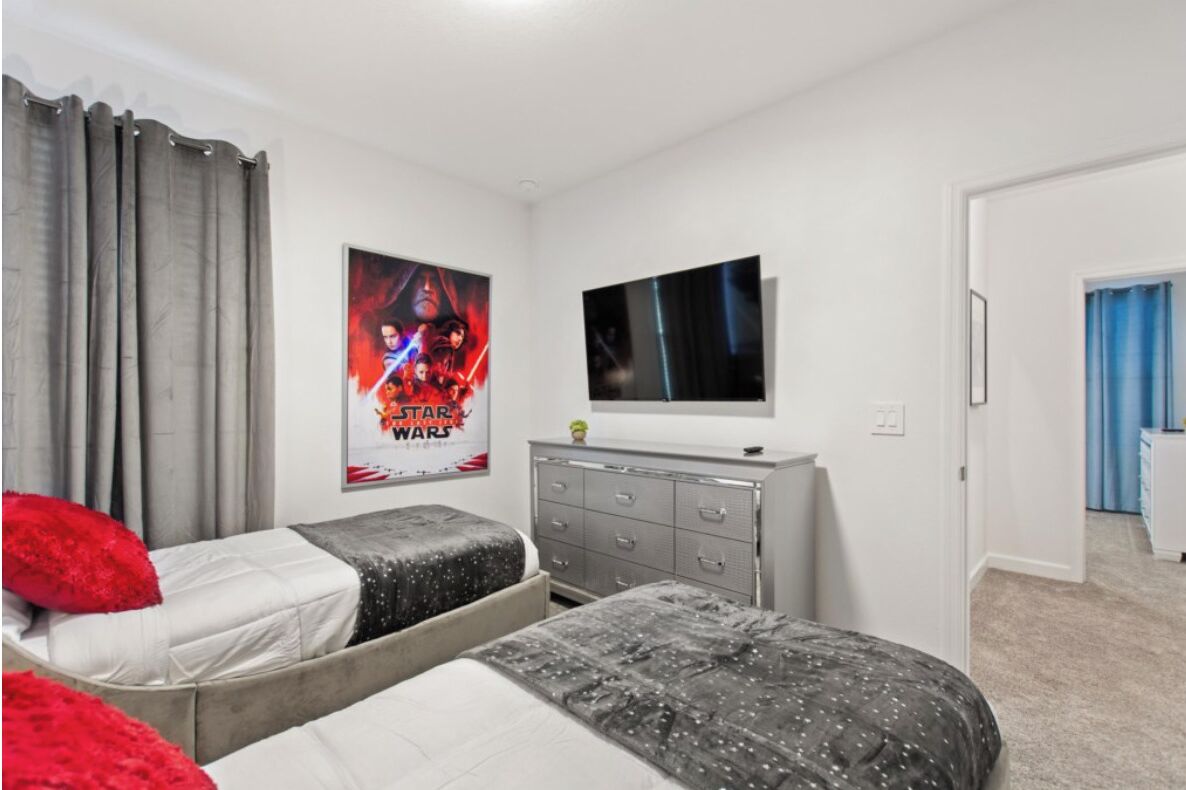 A bedroom with two beds, a dresser, a TV, and Star Wars posters.