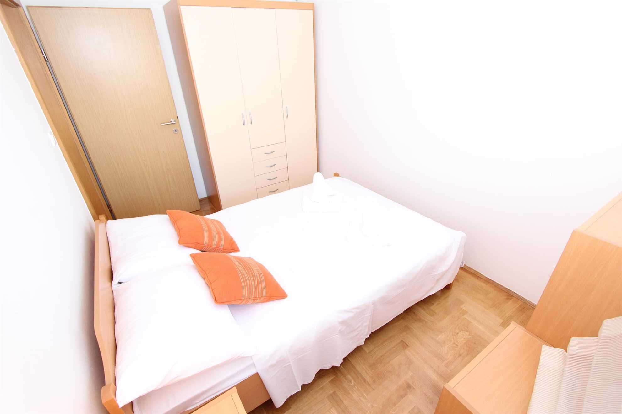 Ein kleines, ordentlich eingerichtetes Schlafzimmer mit einem Einzelbett, einem Holzschrank und einem kleinen Tisch.