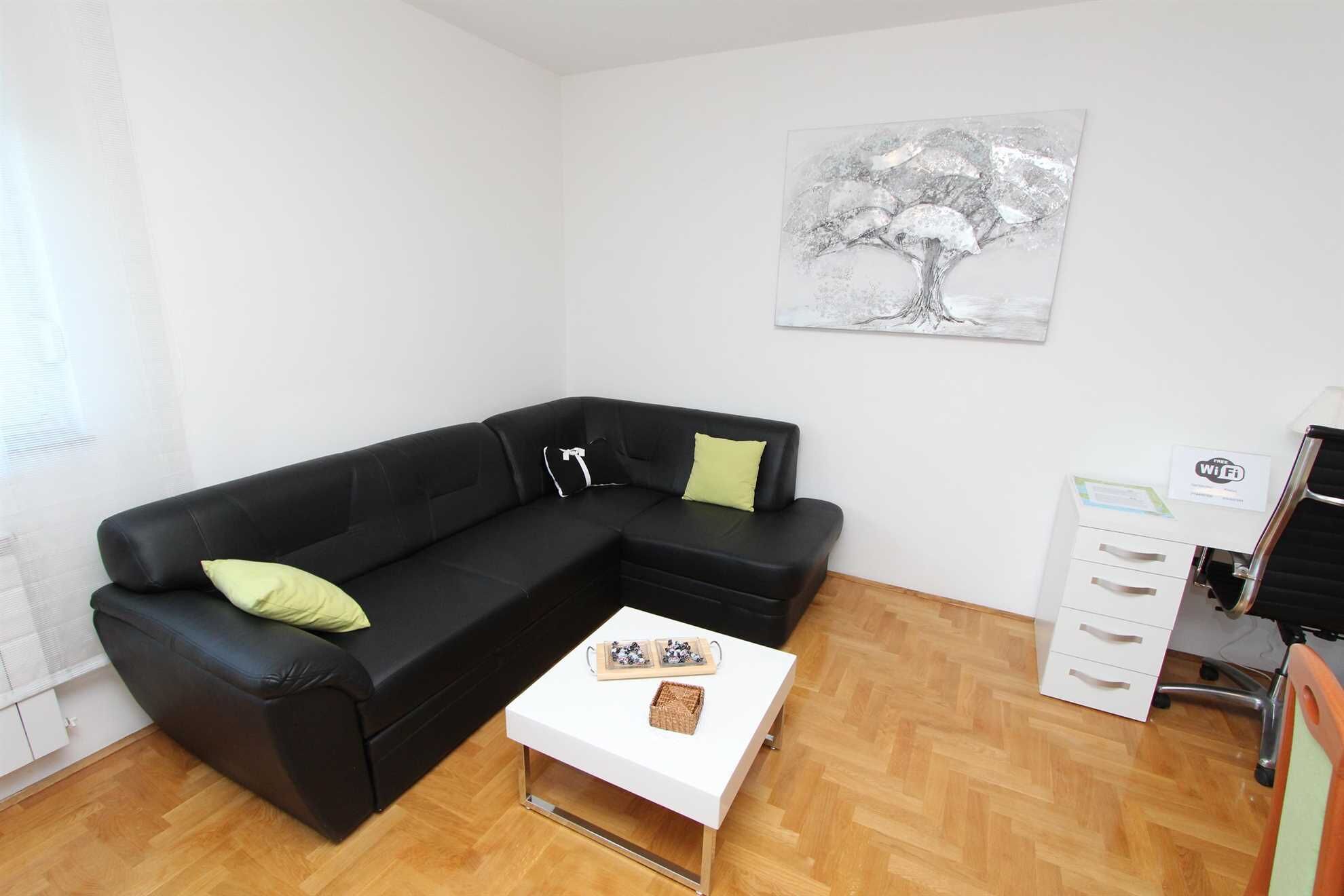 A modern living room with a black leather sofa, a white coffee table, and a white cabinet with drawers.