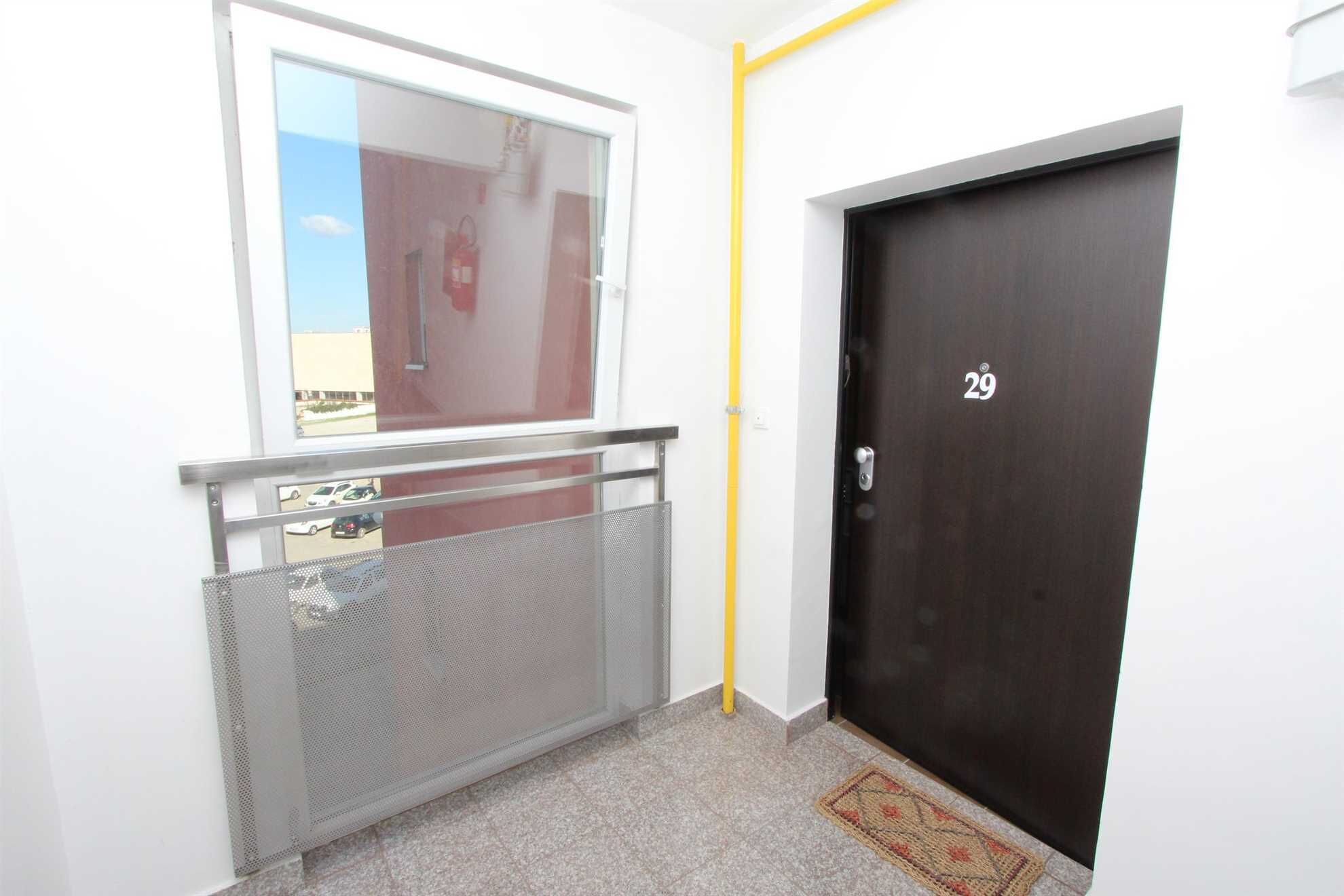 A hallway with a window, a metal gate, a dark door with the number 29, and a yellow pipe.